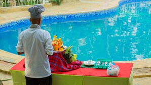 Ein Koch steht an einem Pooltisch mit einer Anordnung tropischer Früchte, einer grünen Tischdecke und einer Wasserflasche.