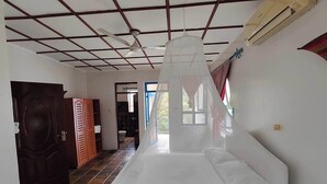 Ein Schlafzimmer mit Bett, Deckenventilator, Klimaanlage, Kleiderschrank und einem durchgegangene Tür erkennbaren Badezimmer.