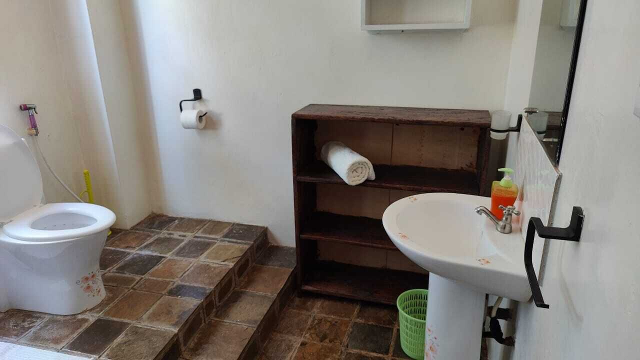 Une salle de bain avec des toilettes, un lavabo, une étagère avec une serviette et un panier vert.