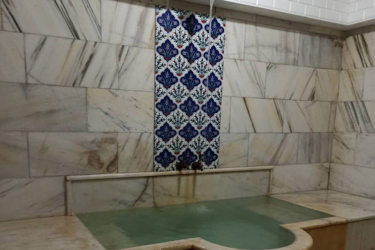 A spa room with a wooden bathtub, marble walls, and a patterned curtain.