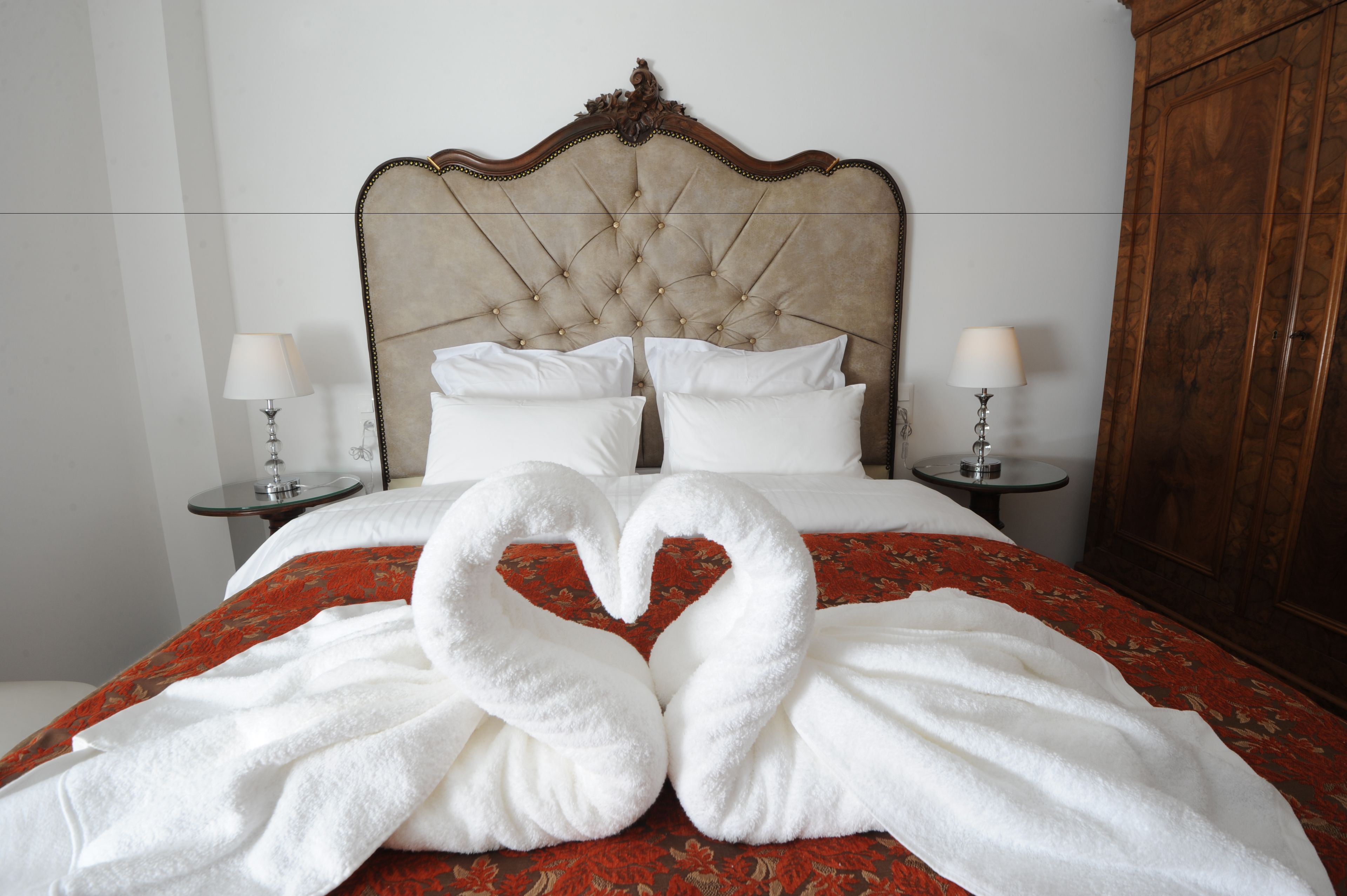 A hotel room with a large bed, two bedside tables, and a wardrobe.