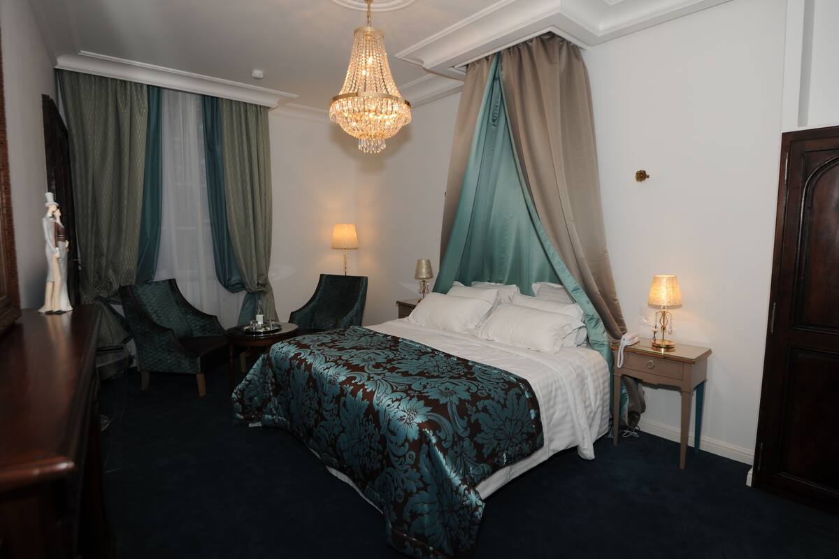 A hotel room with a large bed, two bedside tables, a chandelier, and a desk with a chair.