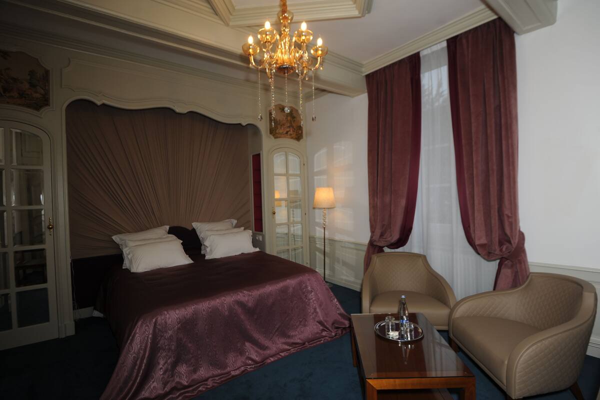 A hotel room with a large bed, a chandelier, a desk, and a chair.