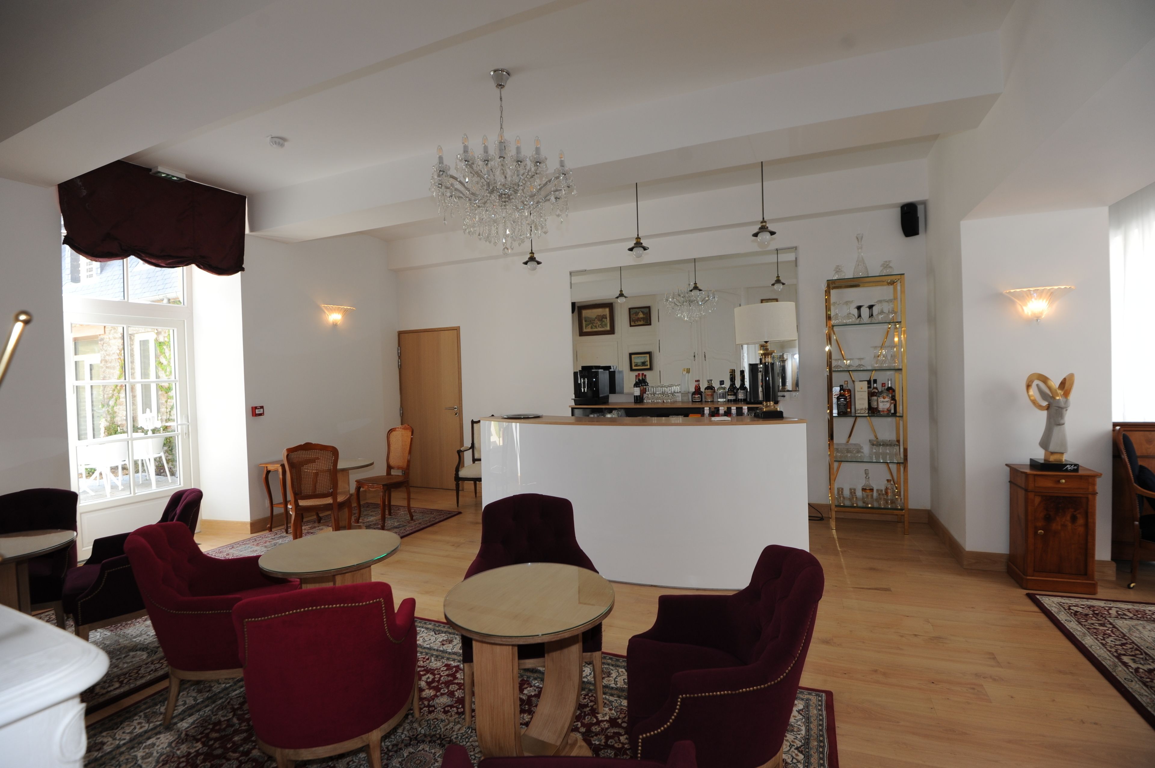 A spacious living area with a central bar, red upholstered chairs, a chandelier, and a view of the kitchen.