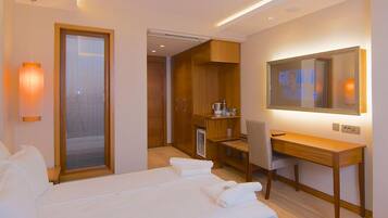 A hotel room with a bed, a desk, a chair, a mirror, and a wardrobe.