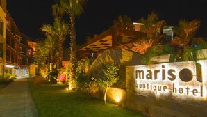 Letrero bien iluminado de un hotel boutique, con un muro de piedra y palmeras al fondo.