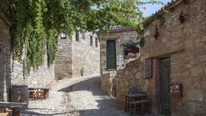 A narrow cobblestone street with stone buildings, wooden tables, and chairs, suggesting a rustic setting. - Hunnaphan Otel (Ayvacik)
