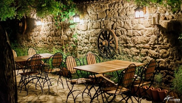 An outdoor dining area with stone walls, wooden tables, and metal chairs. - Hunnaphan Otel (Ayvacik)