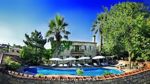 A pool area with lounge chairs and umbrellas, surrounded by trees and a stone building. - Hunnaphan Otel (Ayvacik)