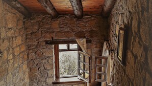 A rustic interior with a wooden staircase, stone walls, and a window with open shutters. - Hunnaphan Otel (Ayvacik)