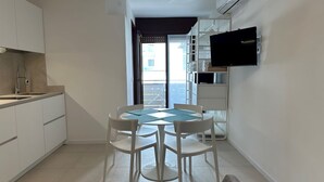 A compact kitchen with white cabinets, a dining table with chairs, and a flat-screen TV mounted on the wall.