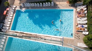 A rectangular swimming pool with clear blue water, surrounded by white lounge chairs and a few people swimming.
