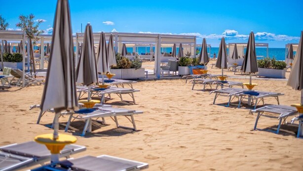 A beachside lounge area with sun loungers and umbrellas, a sandy beach, and a clear view of the sea.