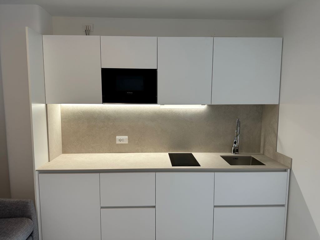 Cocina compacta con gabinetes blancos, un microondas negro, un lavamanos e iluminación debajo de los armarios.