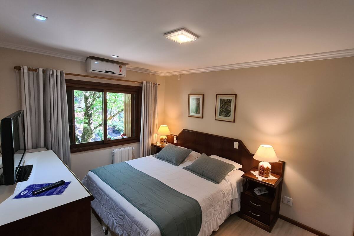 Ein Hotelzimmer mit einem Bett, Nachttischen, einem Schreibtisch, einem Fernseher und einem Fenster mit Vorhängen.