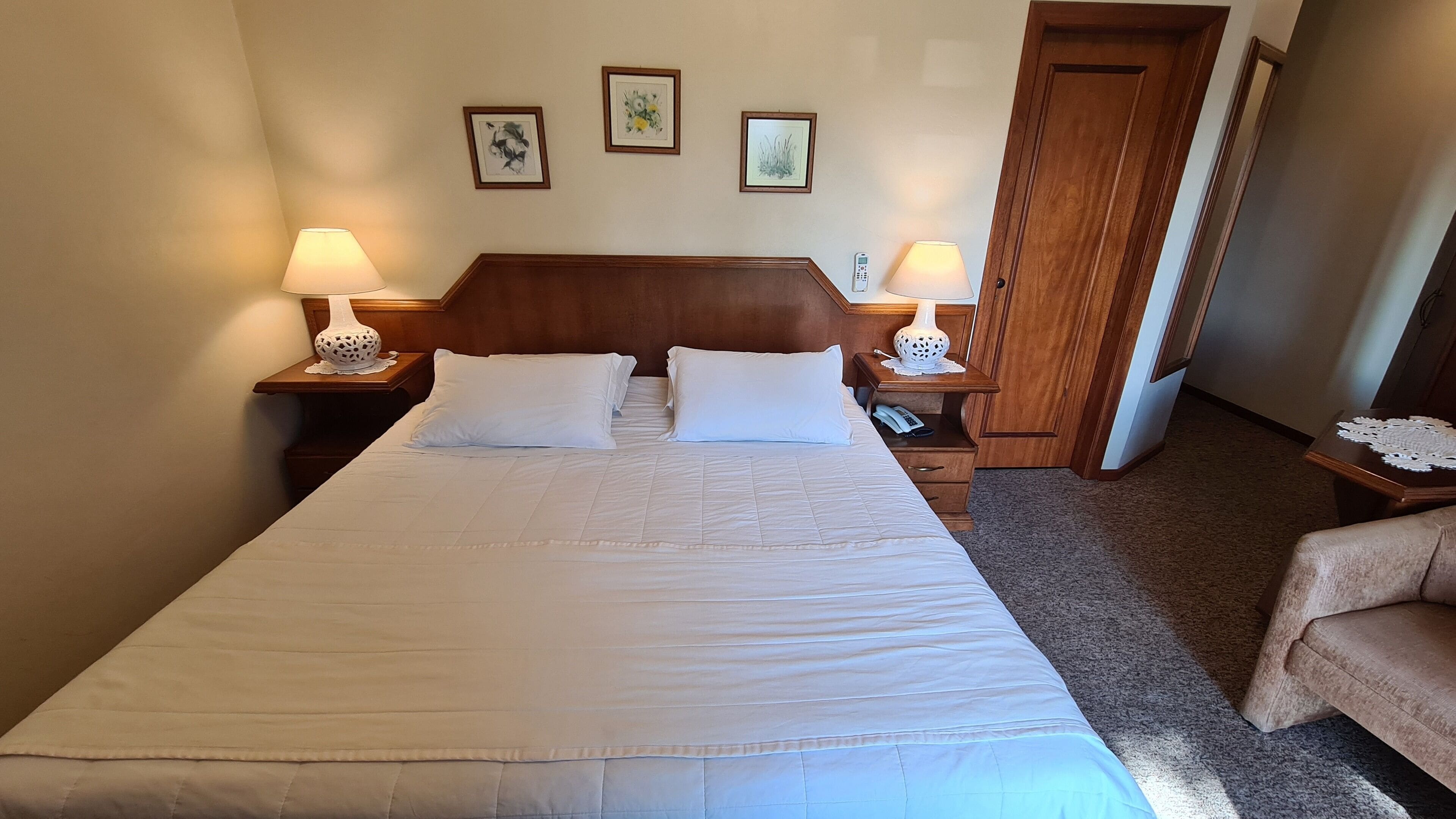 Una cama bien hecha con sábanas blancas, dos mesitas de noche con lámparas y un cabecero de madera.