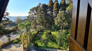 A view from a window overlooking a landscaped garden with a variety of trees and a paved pathway. - Hotel Azaleia (Gramado)