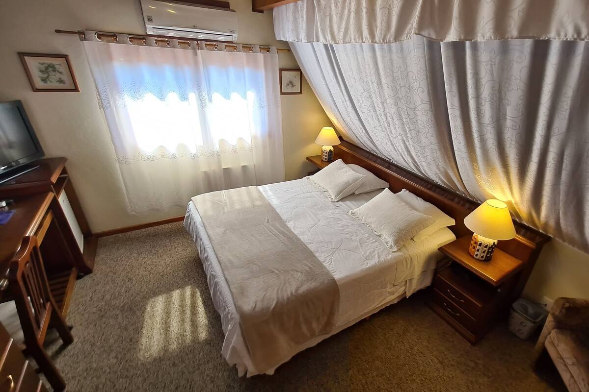 Ein ordentlich eingerichtetes Hotelzimmer mit Bett, Nachttischlampen, einem Fernseher und einem kleinen Schreibtisch.