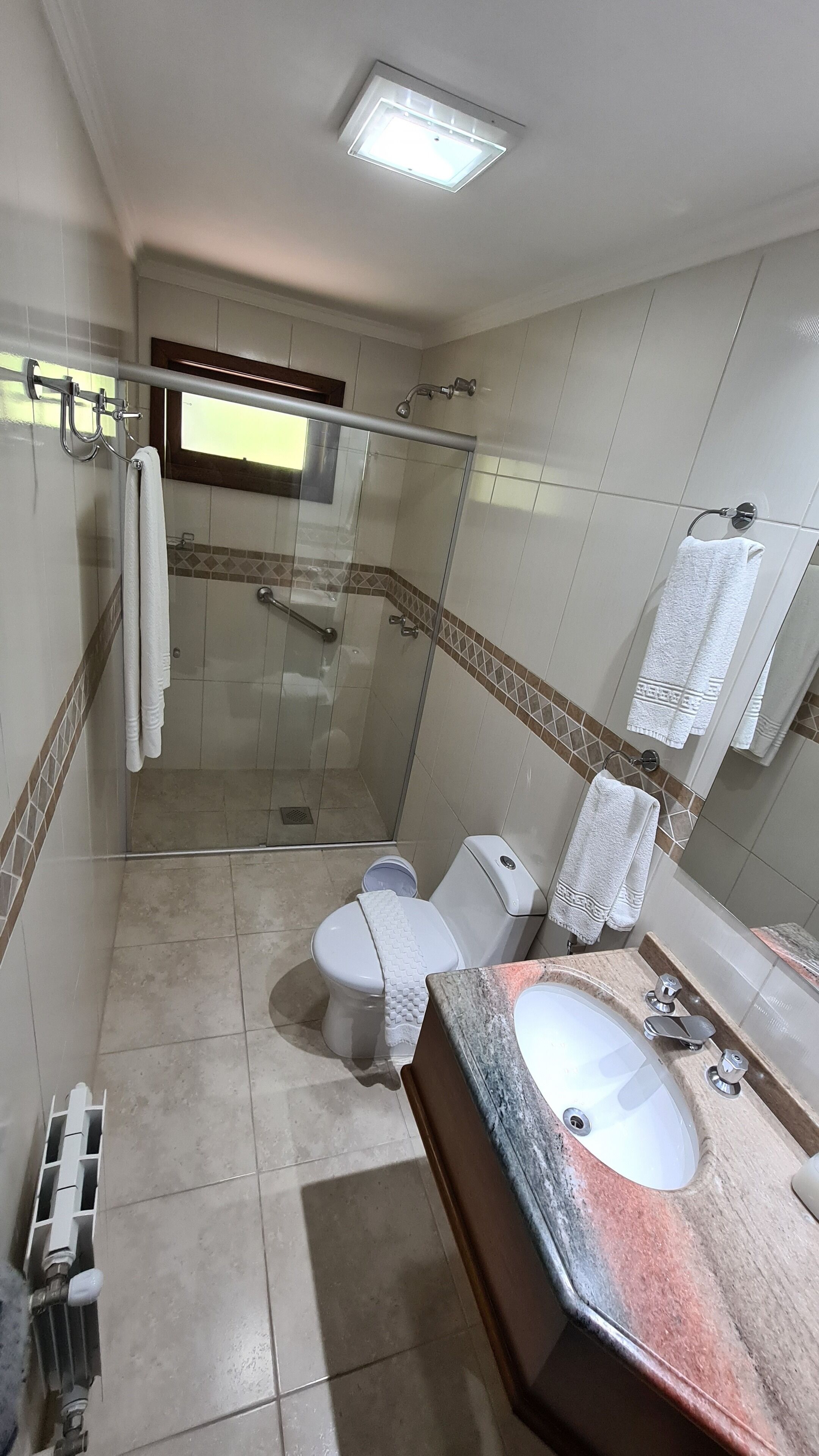 A modern bathroom with a glass-enclosed shower, a white toilet, a sink with a marble countertop, and a mirror.