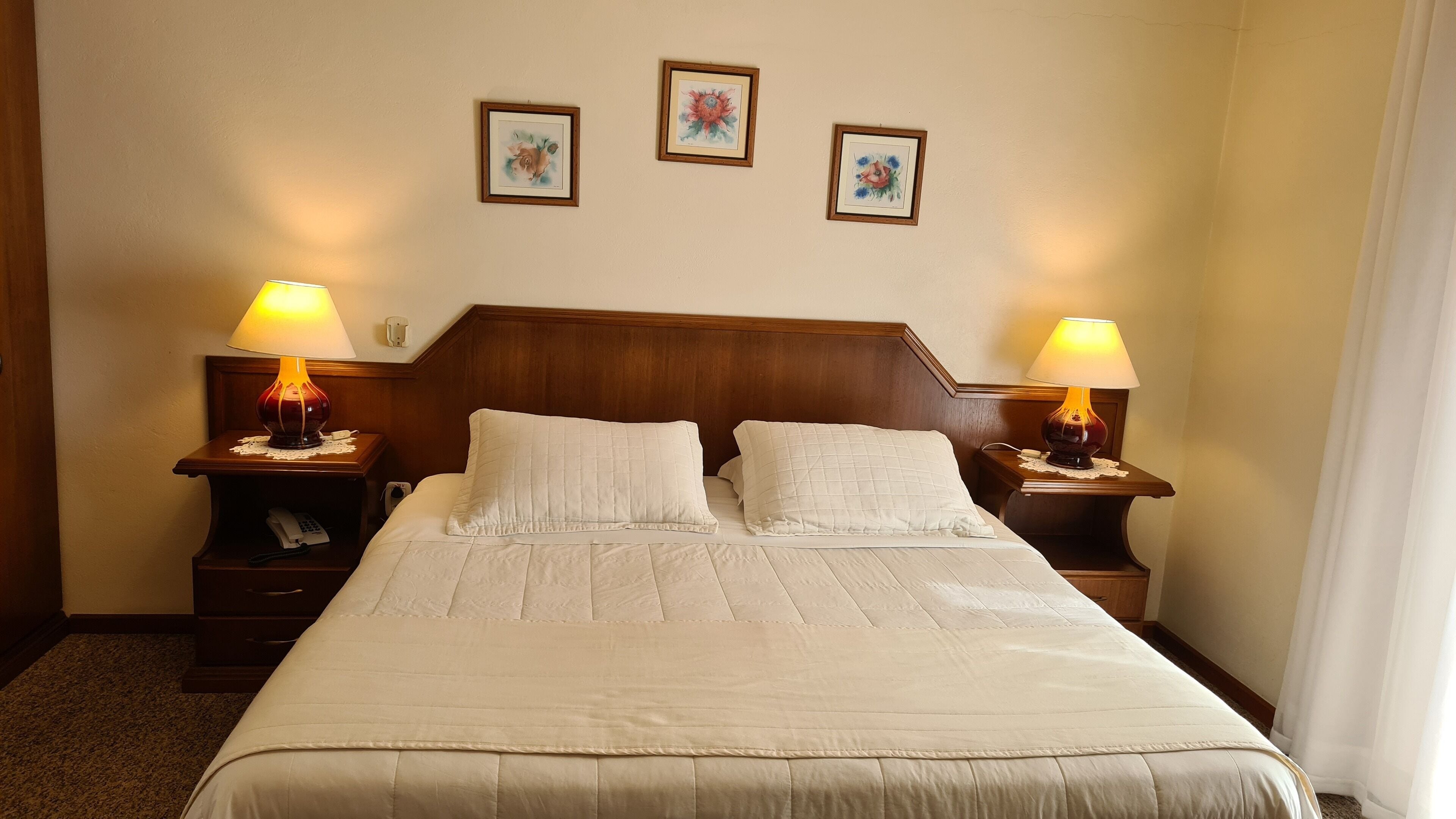 Ein Hotelzimmer mit einem großen Bett, zwei Nachttischlampen und drei gerahmten floralen Kunstwerken an der Wand.