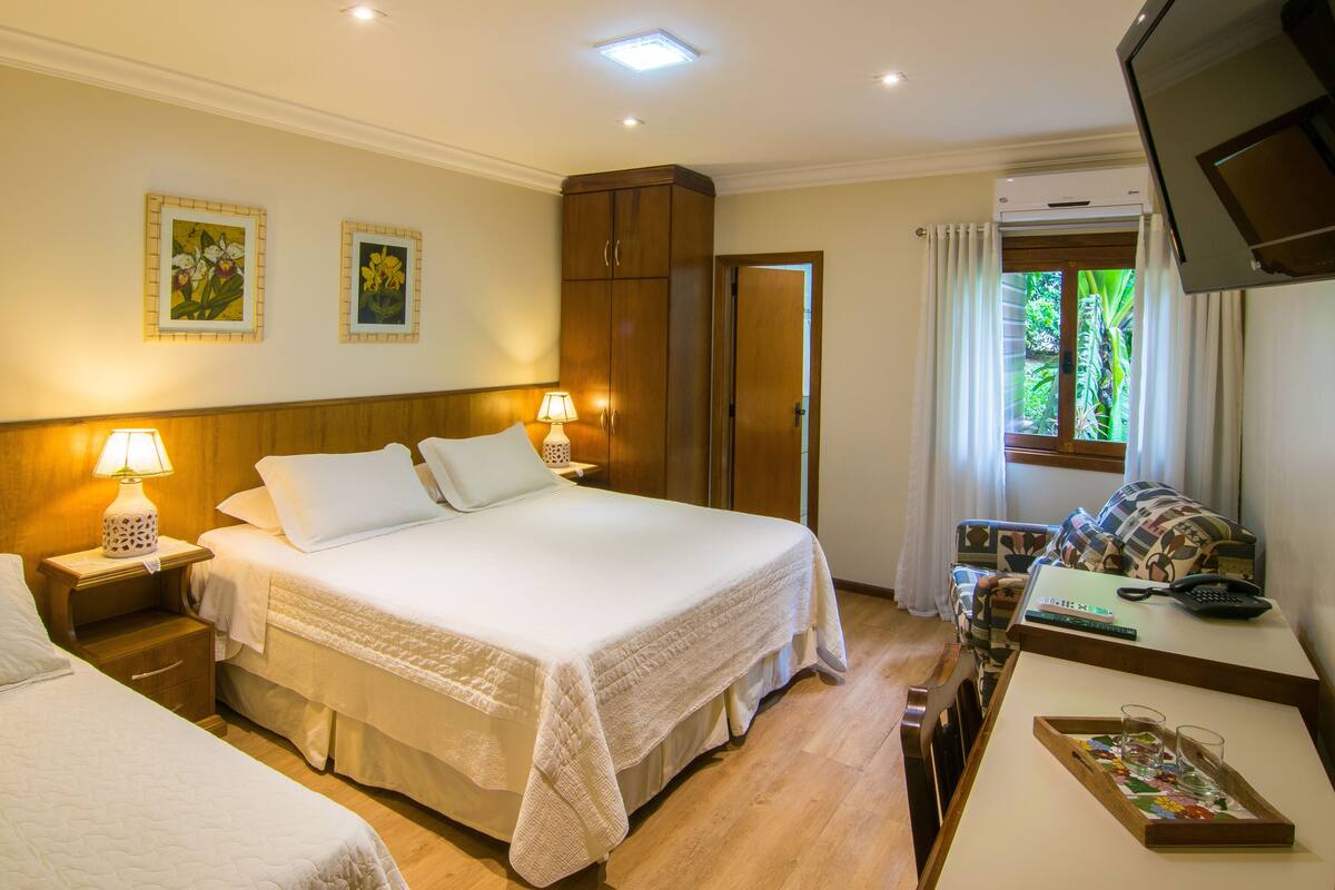 Ein Hotelzimmer mit einem großen Bett, zwei Nachttischen mit Lampen, einem Sofa, einem Schreibtisch mit Telefon und Fernbedienung sowie einem Fenster mit Vorhängen.