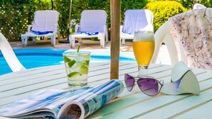 A poolside table with a drink, sunglasses, and a magazine. - Hotel Azaleia (Gramado)