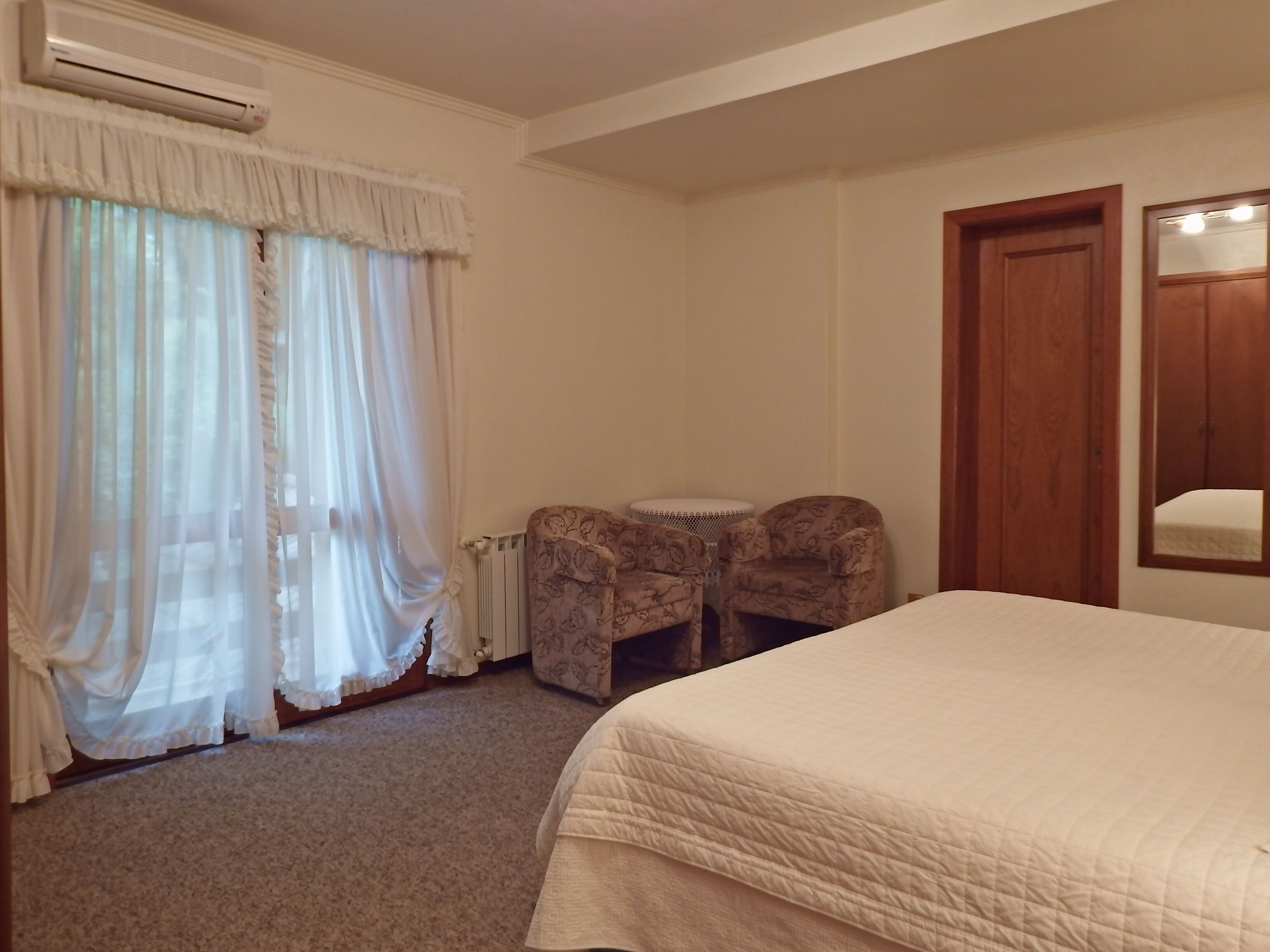 A bedroom with a bed, a radiator, a chair, and a wooden door.