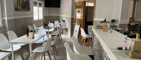 Un espace repas moderne avec des chaises et des tables blanches, un comptoir de bar et un tableau au mur.