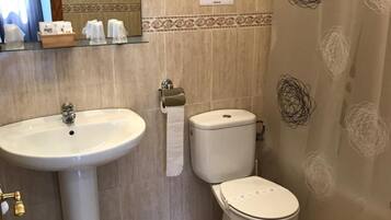 Een badkamer met een wastafel, toilet en bidet. Boven de wastafel hangt een spiegel, en aan de muur is een handdoekdispenser bevestigd.