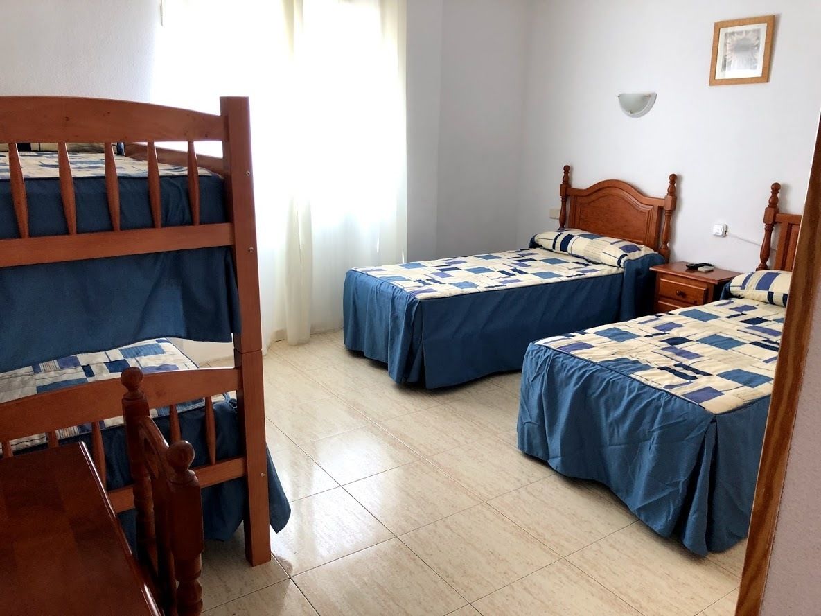 Una habitación con dos literas de madera y una cama individual, todo con ropa de cama azul.