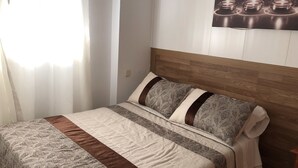 A neatly made bed with patterned bedding, a wooden headboard, and a wall-mounted artwork depicting candles. - Hostal 82 (Olias del Rey)