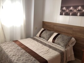 Una cama bien hecha con ropa de cama estampada, un cabecero de madera y una obra de arte colgada en la pared que representa velas.
