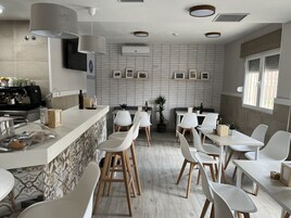 Un café moderno con mostrador, sillas blancas y una máquina de café espresso montada en la pared.