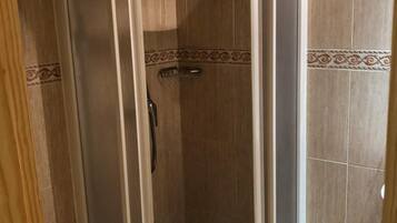 A shower enclosure with a glass door, a showerhead, and a tiled floor.