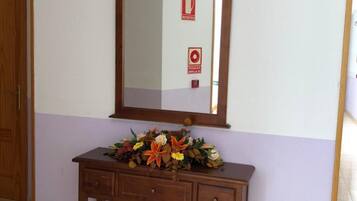 Una consola de madera con un espejo encima, un arreglo floral sobre la mesa y un letrero de seguridad contra incendios en la pared.