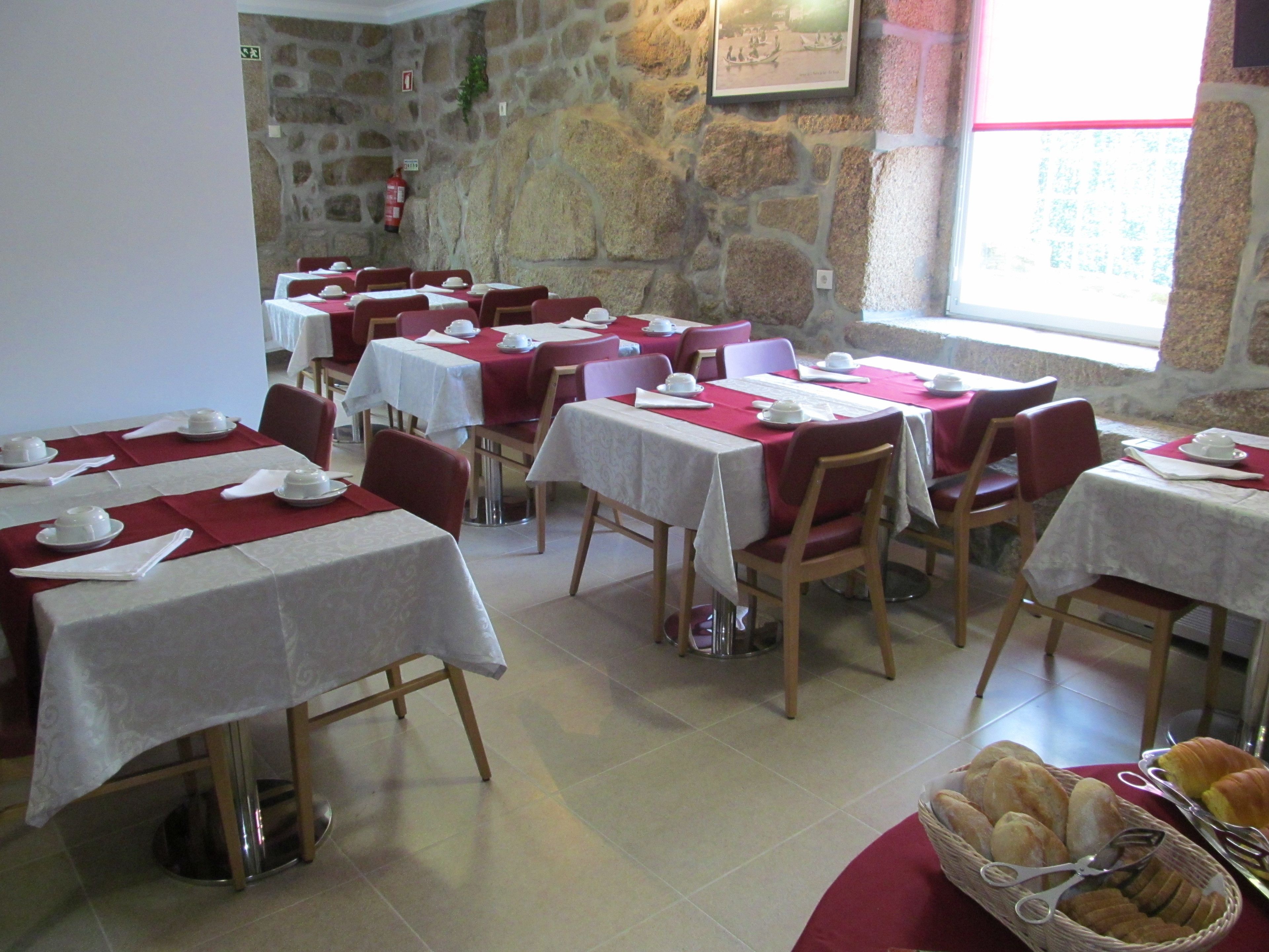 Un restaurant avec plusieurs tables dressées pour le service, des murs en pierre et une fenêtre laissant entrer la lumière naturelle.