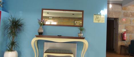 A lobby with a blue wall, a wooden console table, a bench, a chandelier, a potted plant, and a fire extinguisher.