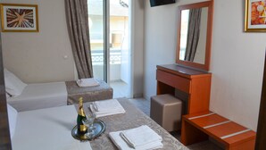 Une chambre d’hôtel avec deux lits, un bureau avec un miroir, un téléviseur fixé au mur et un balcon avec des rideaux.
