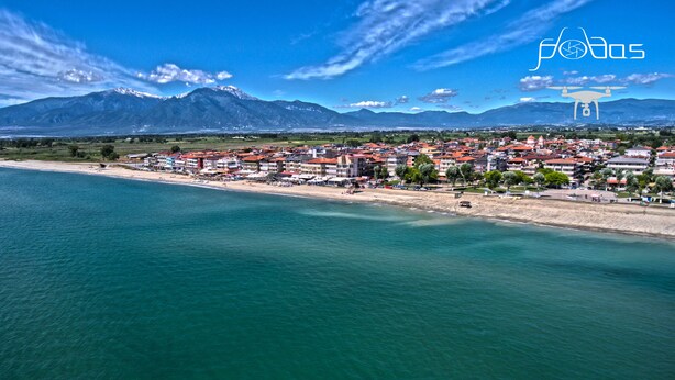 Une ville côtière avec des bâtiments qui bordent la plage, des montagnes en arrière-plan et un ciel dégagé.