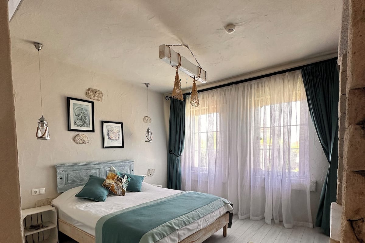 Een slaapkamer met een bed, een nachtkastje, een raam met gordijnen en een hanglamp.