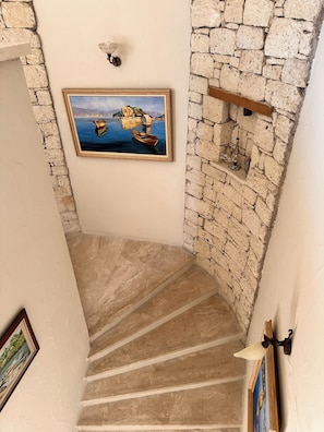 A staircase with stone walls, a framed painting of a boat on water, and a small shelf with a decorative item.