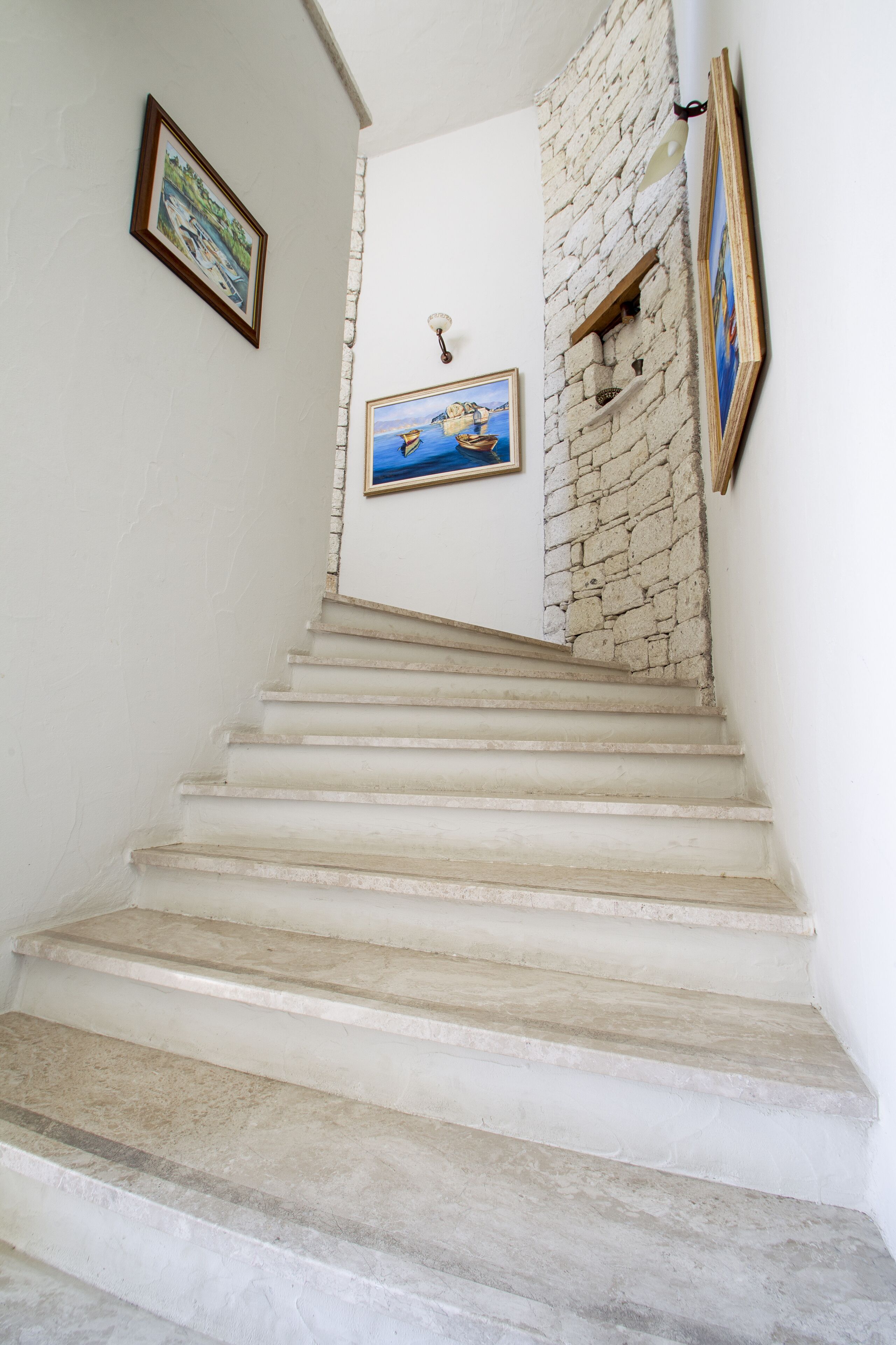 A staircase with white steps leading to a landing with a stone wall and a painting.