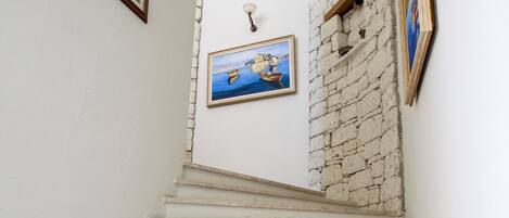 A staircase with white steps leading to a landing with a stone wall and a painting.