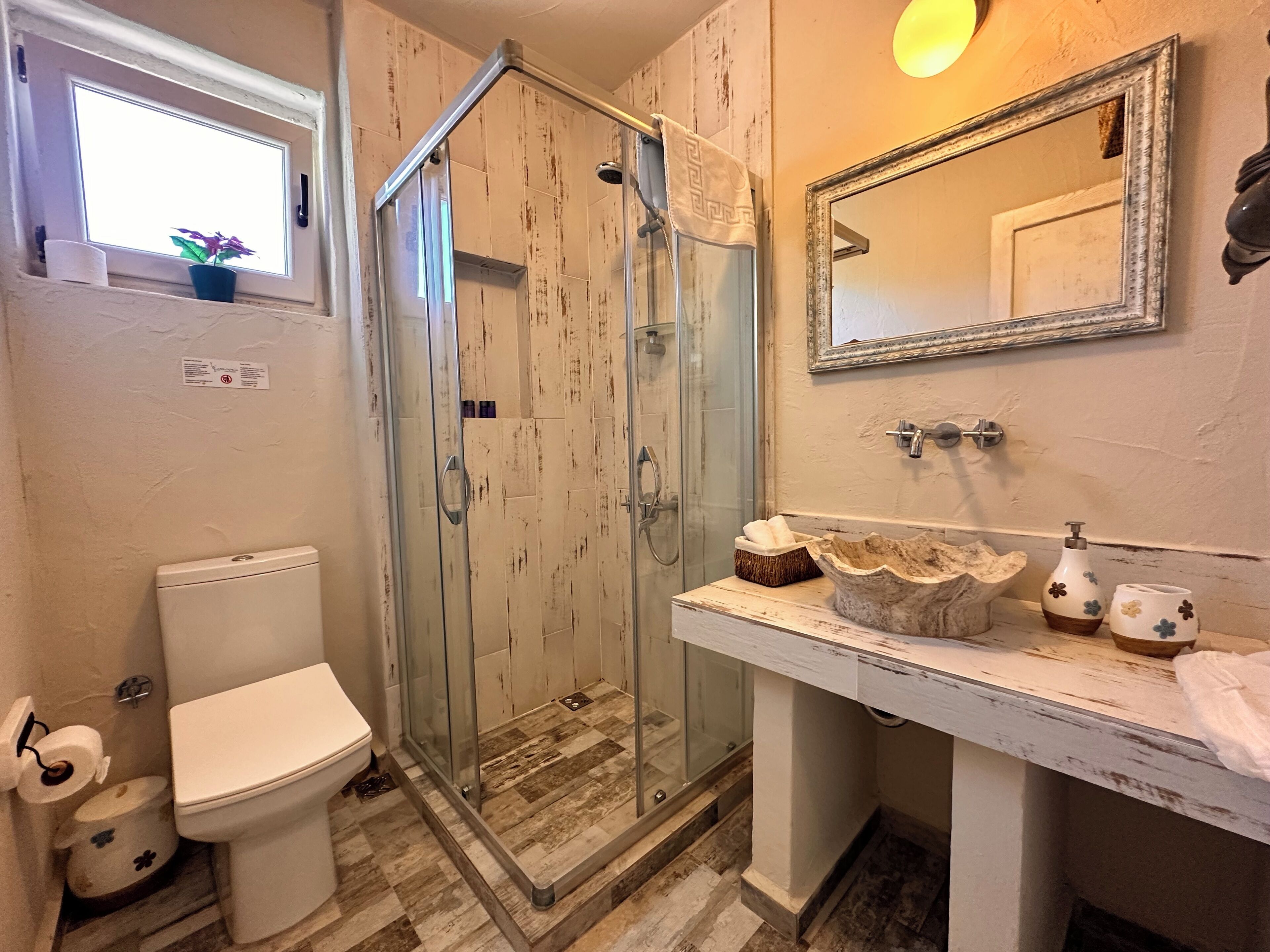 Een badkamer met een douche met glazen wand, toilet, wastafel met decoratieve spullen en een spiegel.