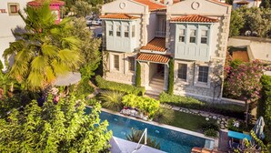 A two-story building with a swimming pool, surrounded by lush greenery and a hilly backdrop. - Cassiopeia Hotel Alacati (Cesme)