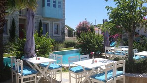 A poolside area with white tables and chairs, a stone building with a red door, and a clear blue sky. - Cassiopeia Hotel Alacati (Cesme)
