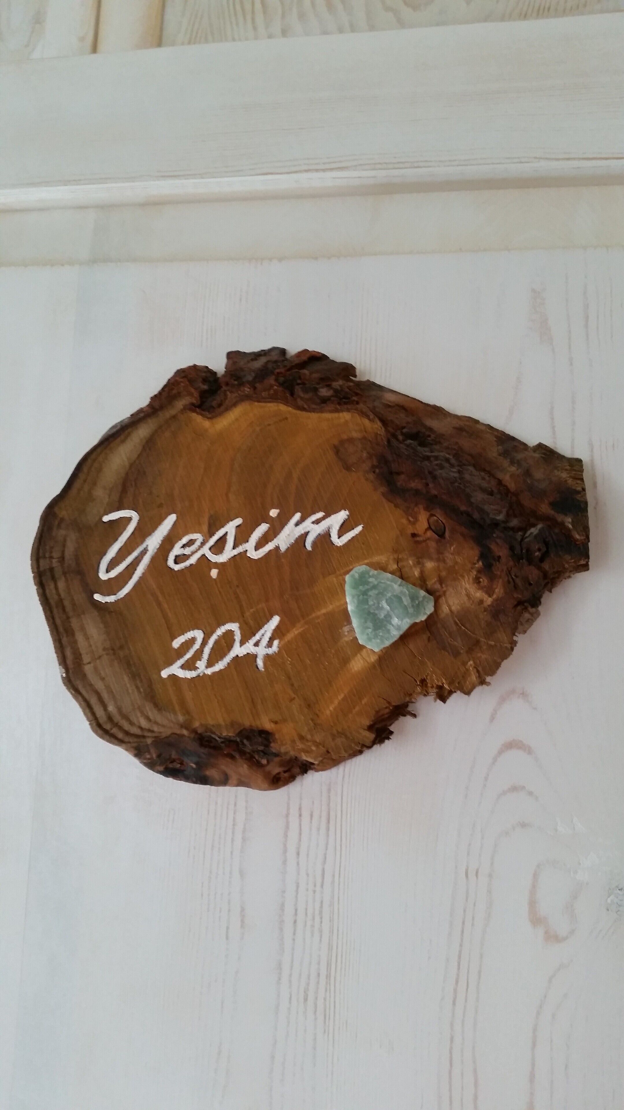 A wooden plaque with the inscription "Yesim 204" on a white wooden surface.