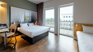 Habitación de hotel moderna con una cama grande, un escritorio con una computadora portátil, una silla y un balcón con vistas a la ciudad.