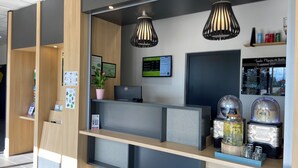 Un mostrador de recepción moderno con una computadora, una planta en maceta y una pantalla digital.