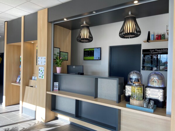 A modern reception desk with a computer, a potted plant, and a digital display.
